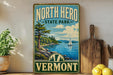 A vintage-style sign for North Hero State Park in Vermont, featuring a scenic landscape with a lake, mountains, and a sailboat.