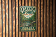 A vintage metal sign for O'Bannon Woods State Park in Indiana, featuring a scenic illustration of a forest and a bridge.