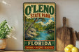 A vintage-style sign for O'Leno State Park in Florida, featuring a scenic landscape with a river and palm trees.