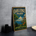 A vintage-style sign for Oakledge Park in Vermont, featuring a scenic image of the park with a lake, a lighthouse, and a building.