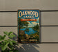 A vintage-style metal sign for Oakwood Lakes State Park in South Dakota, featuring a scenic landscape with a lake, trees, and mountains.