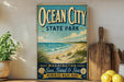 a vintage-style sign for Ocean City State Park, with a beach scene and seagulls in the background, along with a wooden paddle and a potted plant.