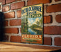 A vintage-style metal sign for Ochlockonee River State Park in Florida, featuring a scenic illustration of the river surrounded by palm trees and a cloudy sky.