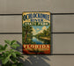 A vintage-style sign for Ochlockonee River State Park, featuring a scenic image of the river surrounded by palm trees and a cloudy sky.