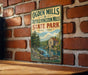 A vintage-style metal sign with text and an illustration of a scenic landscape, mounted on a brick wall.