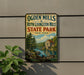 A vintage-style sign for Ogden Mills & Ruth Livingston Mills State Park in New York, featuring a scenic image of a river and a building.