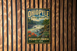 A vintage-style metal sign for Ohio State Park, featuring a waterfall and forest scenery, is displayed on a wooden wall.