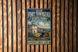 A vintage-style metal sign for Fort Townsend State Park in Washington, featuring a white building with a clock tower and a cannon, mounted on a wooden wall.