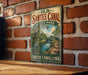 A vintage-style metal sign for the Old Santee Canal State Park in South Carolina is displayed on a brick wall.