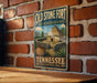 A vintage-style metal sign for Old Stone Fort State Archaeological Park in Tennessee, featuring a depiction of a thatched-roof hut and a palm tree.