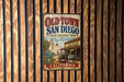 A vintage-style metal sign for Old Town San Diego, California, featuring a historical building and a wagon, is displayed on a wooden wall.