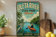 A vintage-style metal sign for Oleta River State Park, Florida, featuring a person kayaking in a river surrounded by palm trees and a city skyline.
