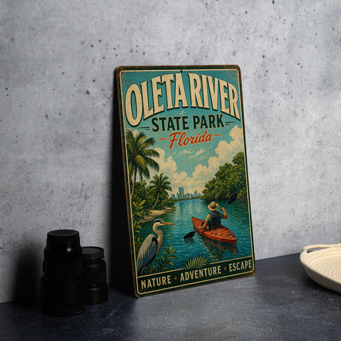 A vintage-style metal sign for Oleta River State Park, Florida, featuring a person kayaking and surrounded by palm trees and a city skyline.