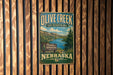 A vintage-style metal sign for Olive Creek State Recreation Area in Nebraska, featuring a scenic landscape with a lake and mountains.