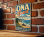 A vintage-style metal sign for Oga Beach State Park in Oregon, featuring a scenic beach landscape with mountains in the background.