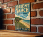 A vintage-style metal sign for Orient Beach State Park in New York, featuring a beach scene with a lighthouse and birds in the sky.