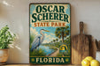 A vintage-style sign for Oscar Scherer State Park in Florida, featuring a large blue heron and palm trees, is displayed on a shelf next to a wooden cutting board and some lemons.