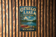 A vintage metal sign for Otsego Lake State Park in Michigan, featuring a scenic illustration of a lake, canoe, and forest.