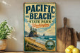 A vintage-style sign for Pacific Beach State Park in Washington, featuring a scenic beach landscape with mountains, trees, and a body of water.