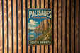 A vintage metal sign for Palisades State Park in South Dakota, featuring a scenic mountain landscape.