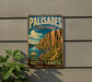 A vintage-style metal sign for Palisades State Park in South Dakota, featuring a scenic landscape with mountains and a river.