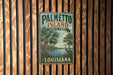 A vintage-style metal sign for Palmetto Island State Park in Louisiana, featuring a palm tree and a bird, mounted on a wooden wall.