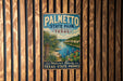 A vintage metal sign for Palmetto State Park in Texas, featuring a scenic landscape with palm trees, a river, and a beach.