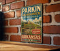 A vintage-style metal sign for Parkin Archeological State Park in Arkansas, featuring a mountain landscape and a pottery bowl.