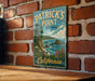 A vintage-style metal sign for Patrick's Point State Park in California, featuring a scenic coastal landscape with rocky cliffs, a beach, and a body of water.