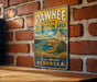A vintage-style metal sign for the Pawnee State Recreation Area in Nebraska, featuring a scenic landscape with mountains, a lake, and sunflowers.