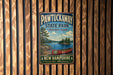 A vintage metal sign for Pawtuckaway State Park, featuring a canoe and a scenic landscape, is displayed on a wooden wall.