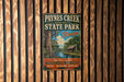 A vintage-style metal sign for Paynes Creek Historic State Park in Florida, featuring a scenic illustration of a river, trees, and a cabin.