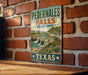 A vintage-style metal sign for Pedernales Falls, a state park in Texas, is displayed on a brick wall.