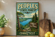 A vintage-style metal sign for the People's State Forest in Connecticut, featuring a scenic landscape with pine trees, a lake, and mountains.