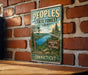 A vintage-style metal sign for the Peoples State Forest in Connecticut, featuring a scenic landscape with pine trees, a lake, and mountains.