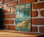 A vintage-style metal sign for Perdido Key State Park, Florida, featuring a beach scene with a crane, palm tree, and turtle.