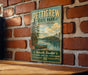 A vintage-style metal sign for Pettigrew State Park, North Carolina, featuring a scenic image of a lake and a canoe, mounted on a brick wall.