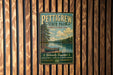 A vintage metal sign for Pettigrew State Park in North Carolina, featuring a scenic image of a lake with a canoe, is displayed on a wooden wall.