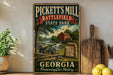 A vintage-style metal sign for Pickett's Mill Battlefield State Park in Georgia, featuring a cannon, a wooden sign, and a scenic landscape.