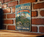 a vintage-style metal sign with a mountain landscape and text, mounted on a brick wall.