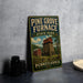 A vintage-style metal sign for Pine Grove Furnace State Park in Pennsylvania, featuring an illustration of a red brick building and a barn surrounded by trees.