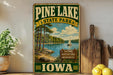 A vintage-style sign for Pine Lake State Park in Iowa, featuring a scenic image of a lake, trees, and a sailboat.