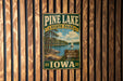 A vintage-style metal sign for Pine Lake State Park in Iowa, featuring a scenic landscape with a lake, trees, and a sailboat.
