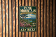 A vintage-style metal sign for Pine Mountain State Resort Park in Kentucky, featuring a scenic landscape with a pine tree, mountains, and a lake.
