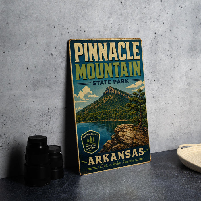 A vintage-style metal sign for Pinnacle Mountain State Park in Arkansas, featuring a scenic mountain landscape and water.