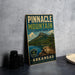 A vintage-style metal sign for Pinnacle Mountain State Park in Arkansas, featuring a scenic mountain landscape and water.