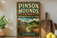 A vintage-style sign for Pinson Mounds State Archaeological Park in Tennessee, featuring an illustration of a bird, a pot, and a road.