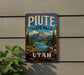 A vintage-style metal sign for Piate State Park, featuring a mountain landscape and a lake, is displayed on a wall.
