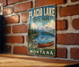 A vintage-style metal sign for Placid Lake State Park in Montana, featuring a scenic landscape with a lake, mountains, and a canoe.