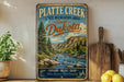 A vintage-style sign for Plate Creek State Recreation Area in South Dakota, featuring a scenic landscape with a river and mountains.
